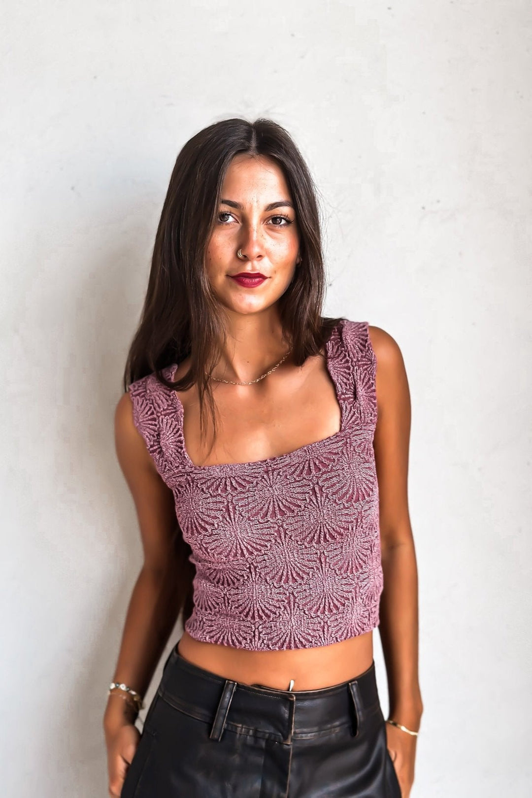 Woman in a purple crop top and black leather pants against a white wall.