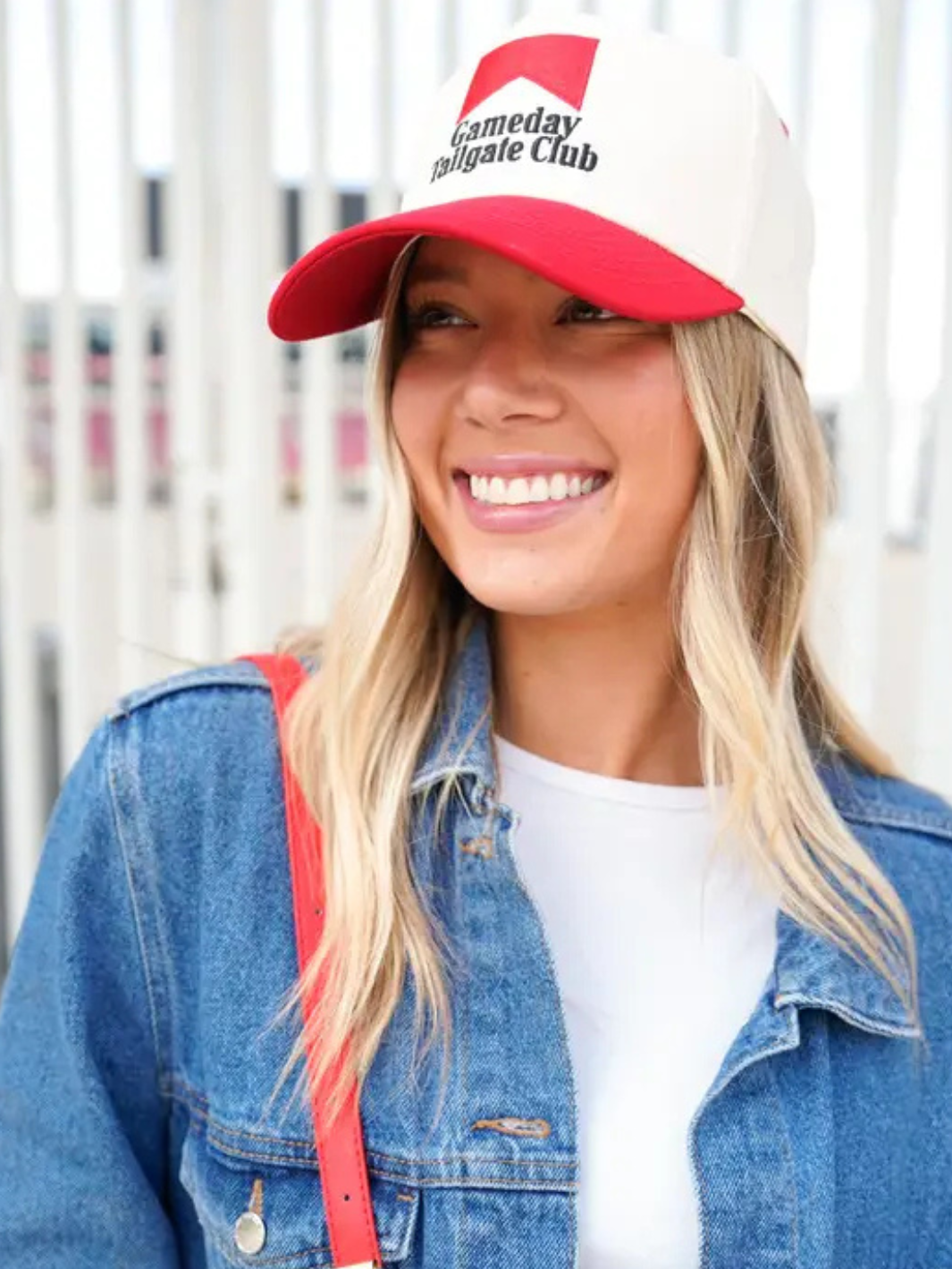 Smiling woman wearing a red-and-cream vintage trucker hat with Gameday Tailgate Club logo.