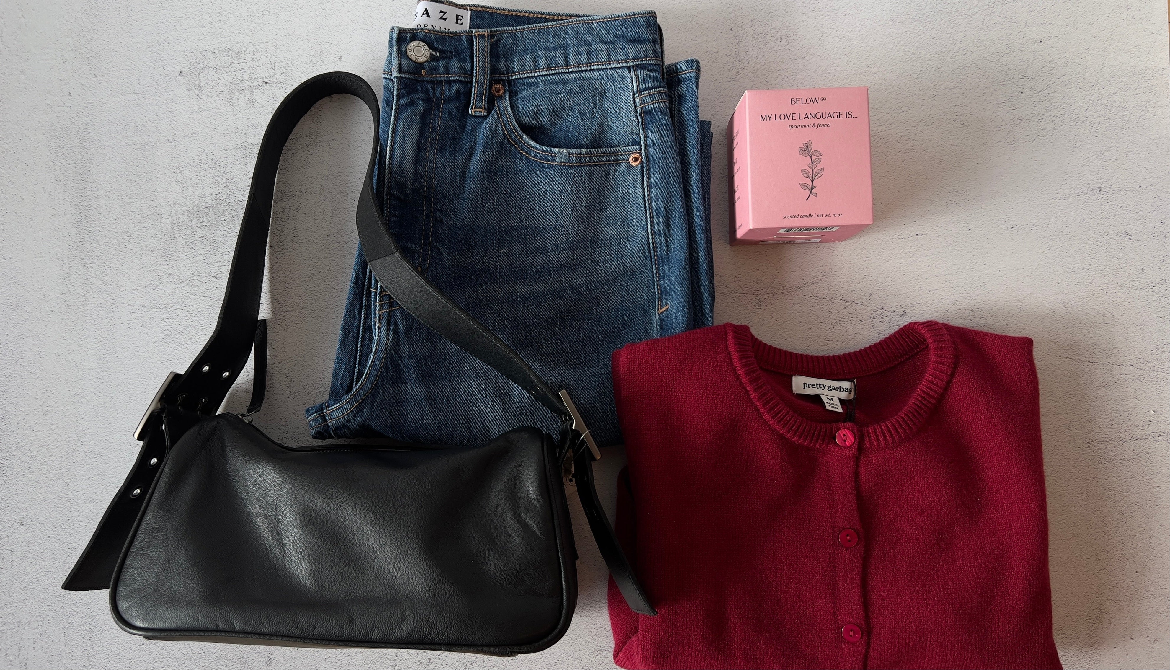 Black handbag, blue jeans, and red sweater on a light gray surface