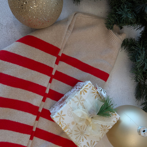 Beige sweater with red stripes on a red and white striped blanket, surrounded by Christmas decorations.