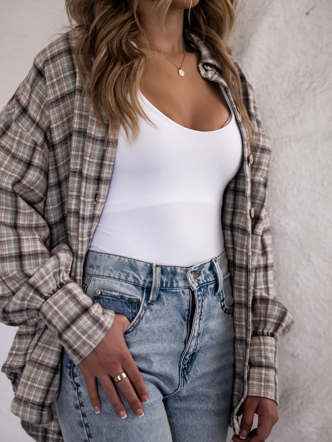 Person wearing a plaid shirt over a white top and jeans against a neutral background