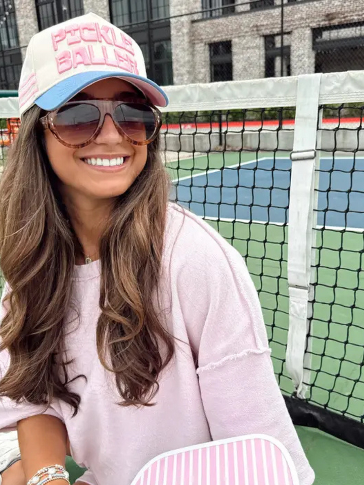 Smiling woman wearing KENZKUSTOMZ Pickleballer Vintage Trucker Hat with front pink 3D Pickle Baller embroidery.