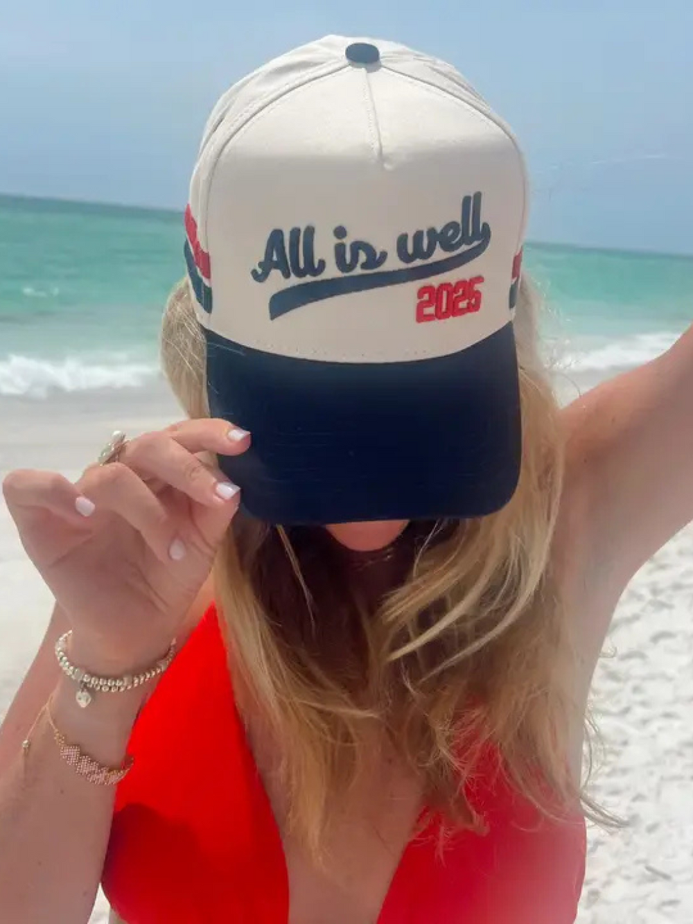 Stylish woman wearing the KENZKUSTOMZ - All is Well Trucker Hat, enjoying a beach day with a positive vibe.