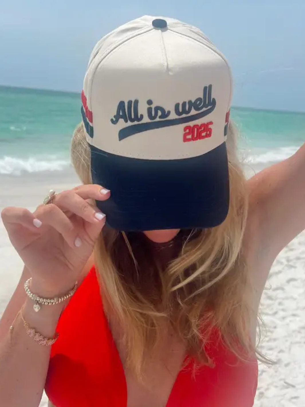 Stylish woman wearing the KENZKUSTOMZ - All is Well Trucker Hat, enjoying a beach day with a positive vibe.