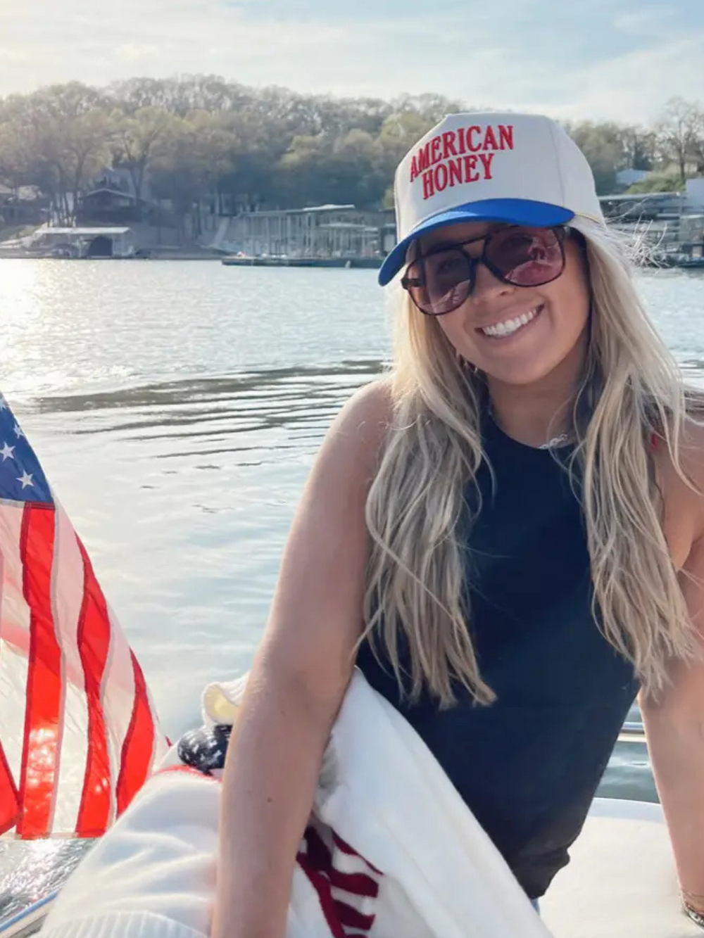 Stylish woman wearing the KENZKUSTOMZ - American Honey Trucker Hat by the water, showcasing its trendy design.