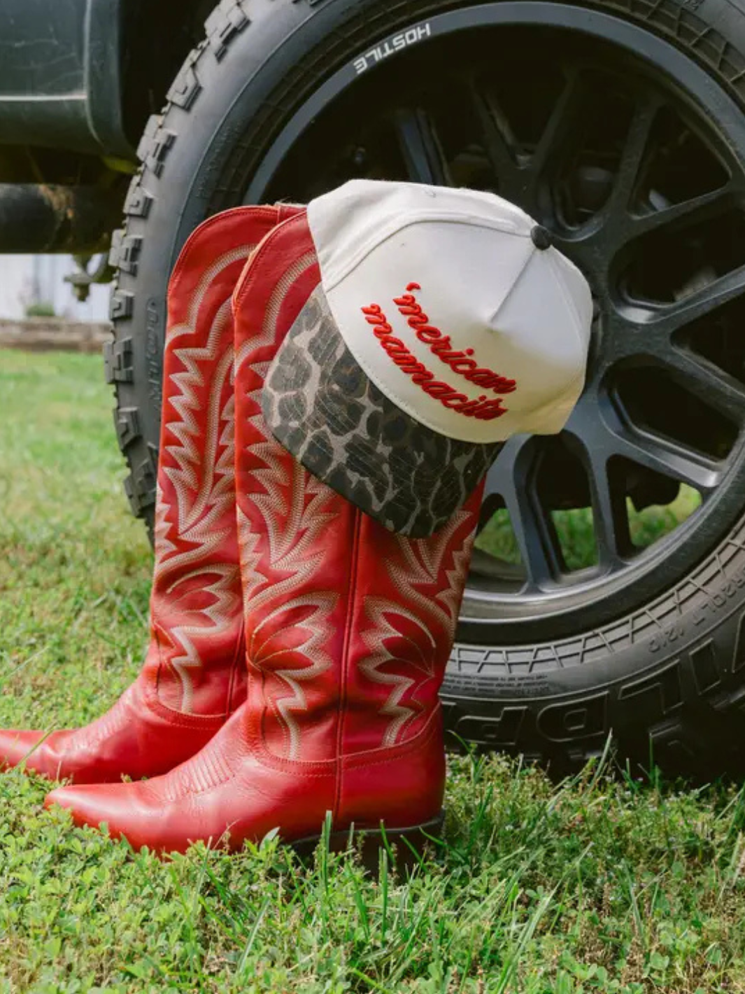 KENZKUSTOMZ - 'Merican Mamacita trucker hat paired with vibrant red cowboy boots against a tire backdrop.