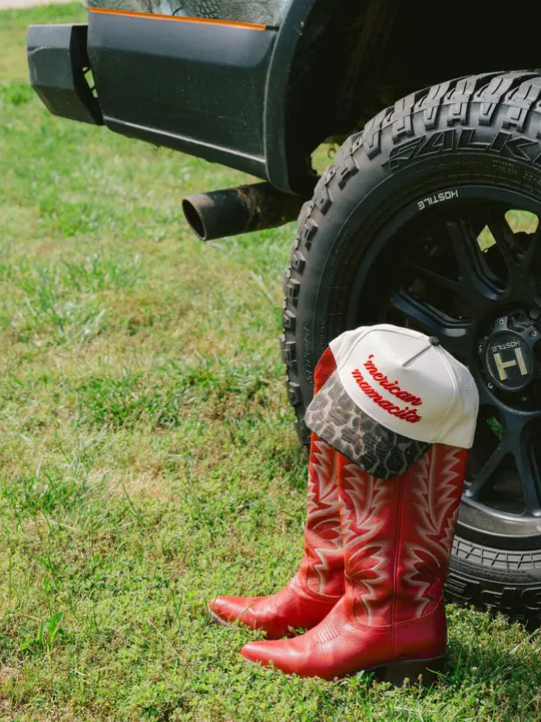 Bold red cowboy boots beside a vintage truck, showcasing the KENZKUSTOMZ - 'Merican Mamacita trucker hat.