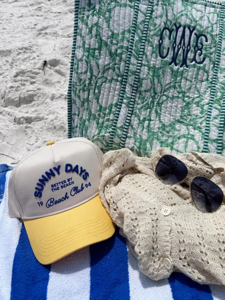 KENZKUSTOMZ - Sunny Days Yellow Vintage Trucker Hat rests on a beach towel, perfect for sun-filled days by the shore.