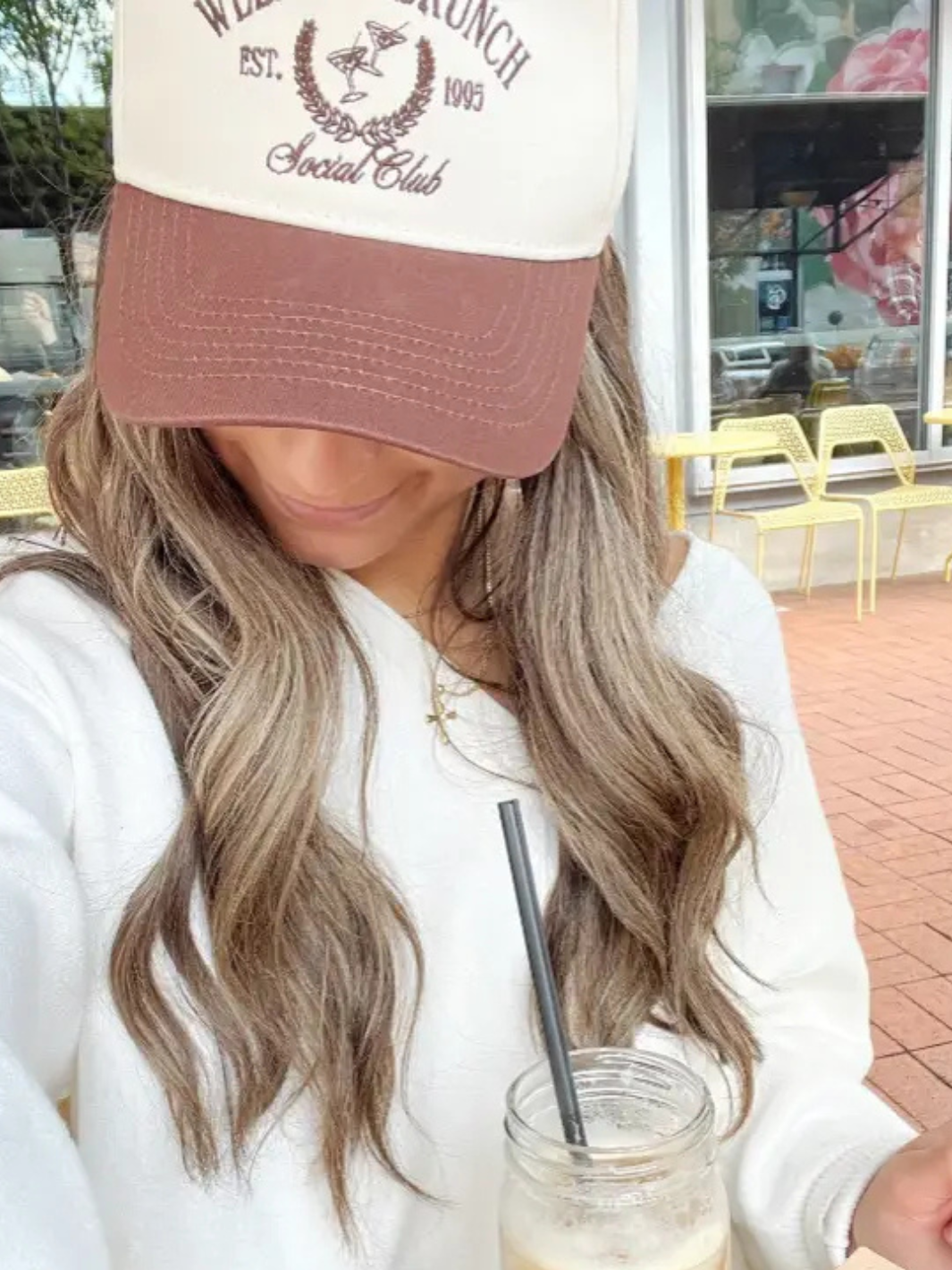 Stylishly wearing the KENZKUSTOMZ - Weekend Brunch Club Trucker Hat while enjoying a drink outdoors.