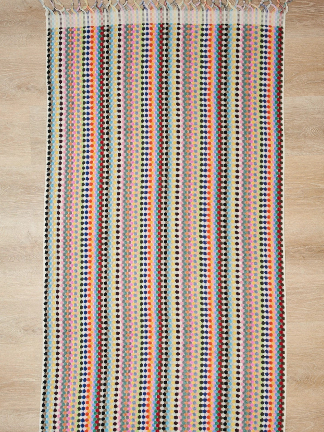 Local Beach Riviera Towel with bright multicolor stripes and fringe on wood floor