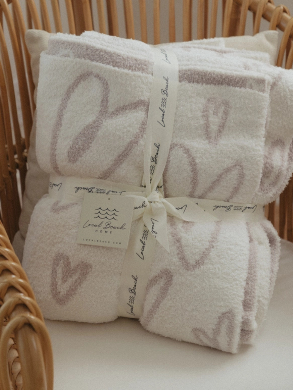 Local Beach Love Heart Luxe Home Blanket, oversized reversible throw in white with pink hearts, folded in a basket.