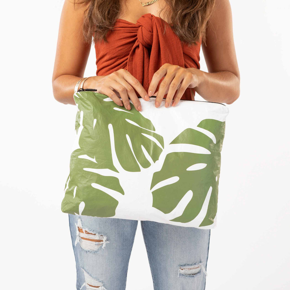Woman in a rust top holding the Monstera MAX Pouch in seaweed green and white
