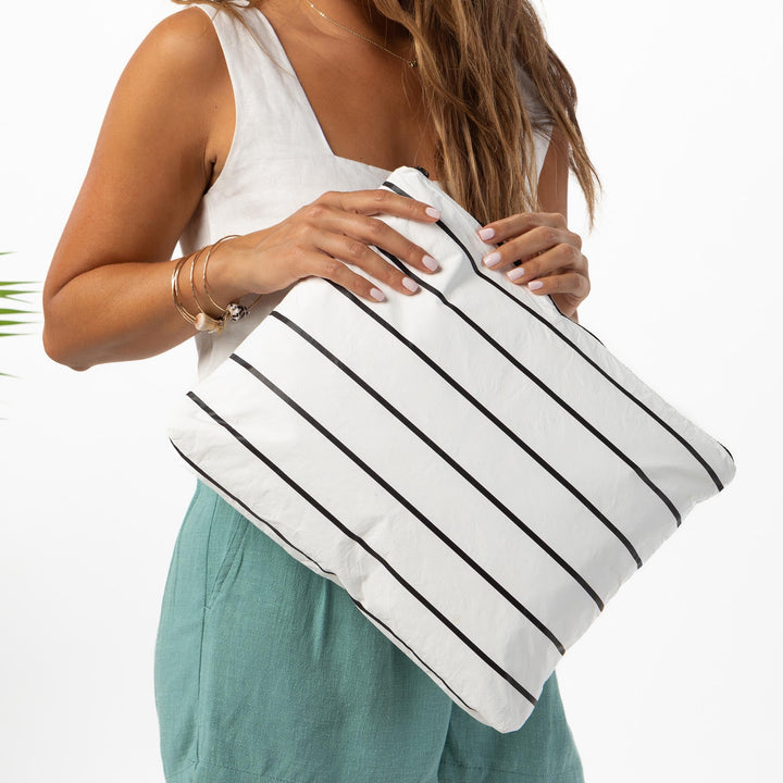 Hands holding the black-and-white striped Pinstripe MAX Pouch against sage-green trousers
