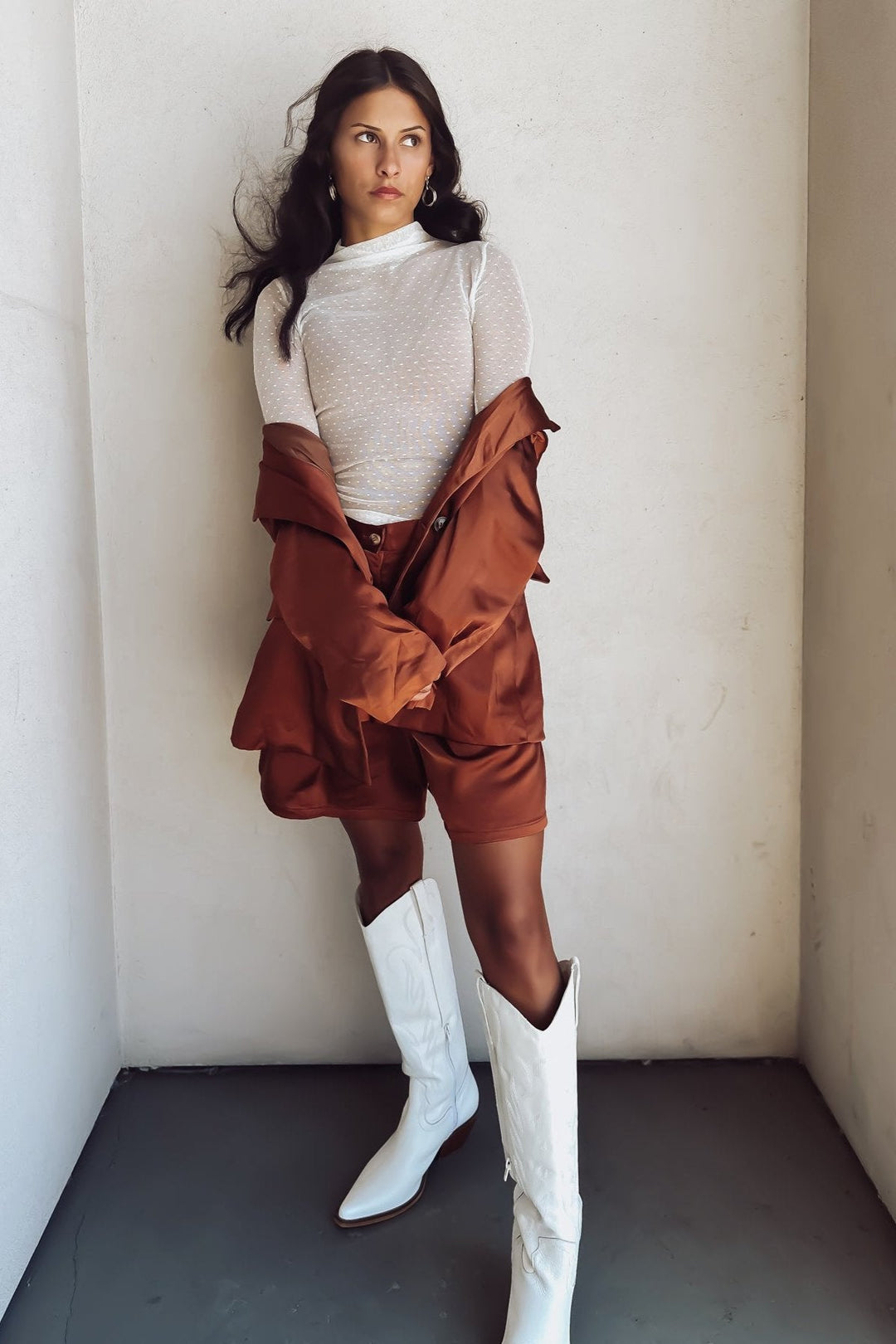 Woman in a bronze-colored blazer over a white top, posing against a white wall.