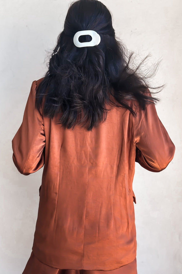 Woman in a bronze-colored blazer over a white top, posing against a white wall.