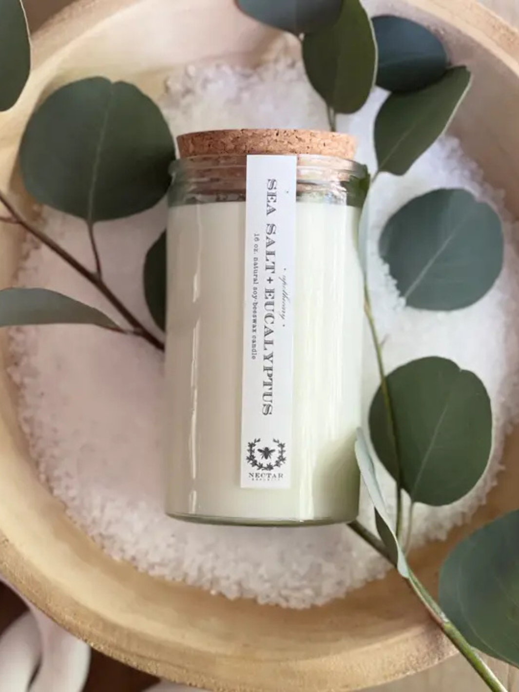 NECTAR REPUBLIC 16oz Sea Salt + Eucalyptus candle in glass jar with cork lid and label, surrounded by eucalyptus leaves.