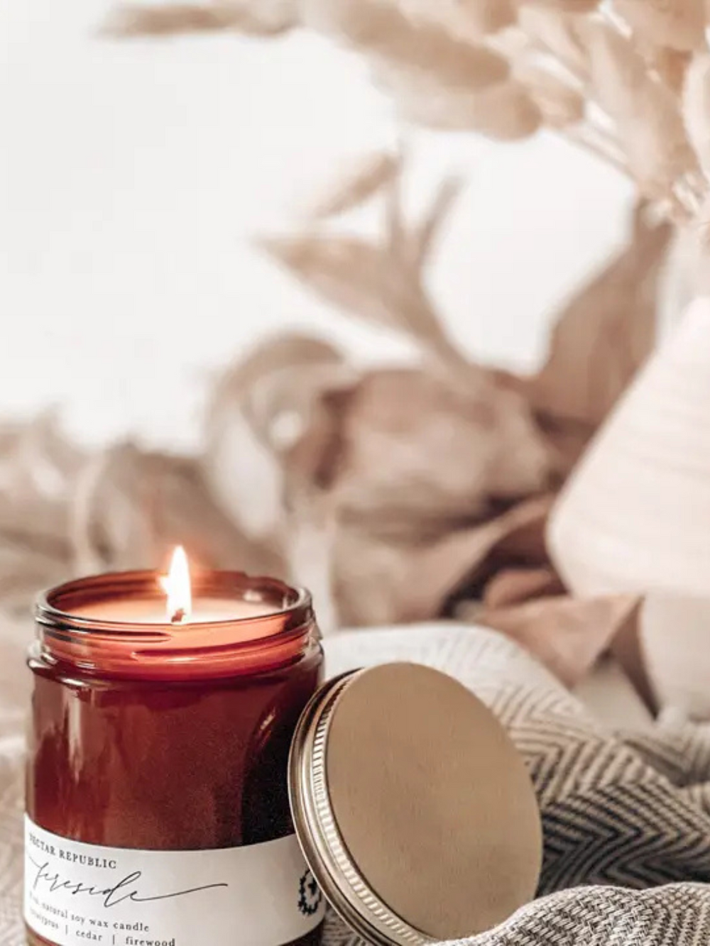 Nectar Republic Fireside 8 oz soy candle in a brown jar, lit beside a cozy blanket.