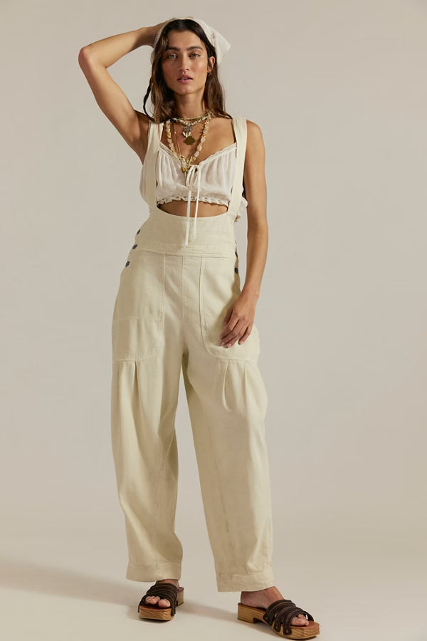 Model wearing FREE PEOPLE The Felix Tapered Overalls in cream with a pinafore-style bodice and wide, tapered legs.