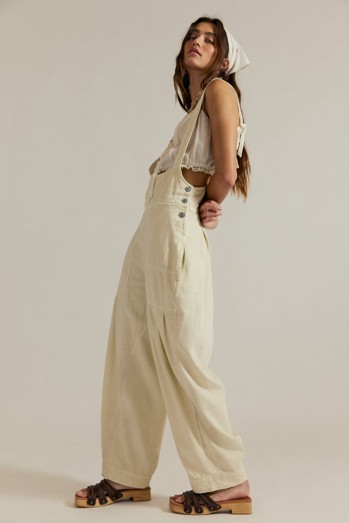 Model wearing cream We The Free Felix Tapered Overall with a slim pinafore bodice and wide legs.