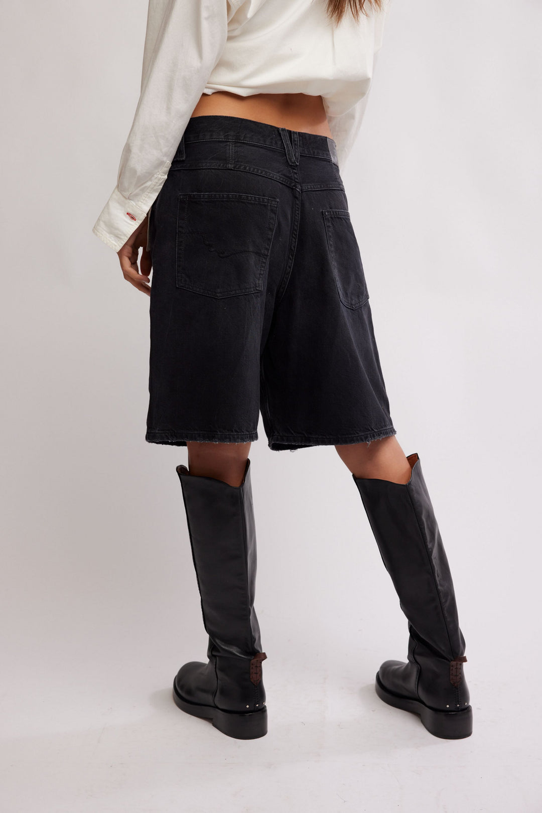 FREE PEOPLE The Montana Short in black denim, mid-rise relaxed Bermuda, back pockets, frayed hem, paired with knee-high boots.