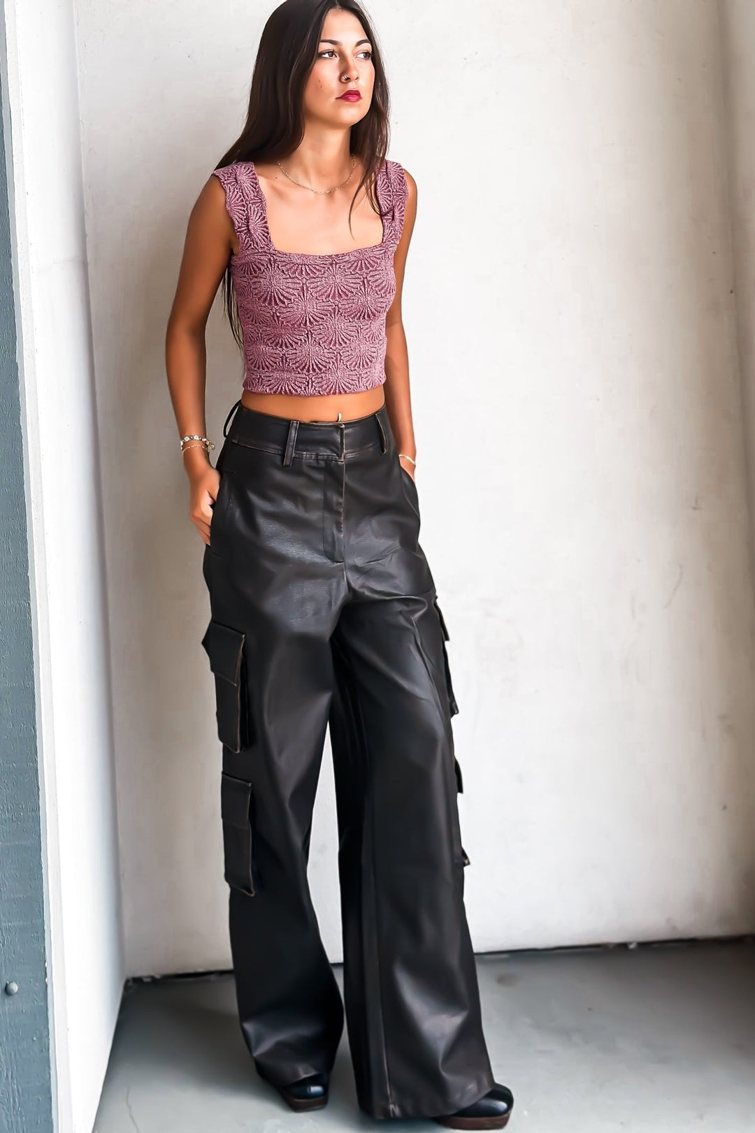 Woman in a purple crop top and leather pants against a white wall.