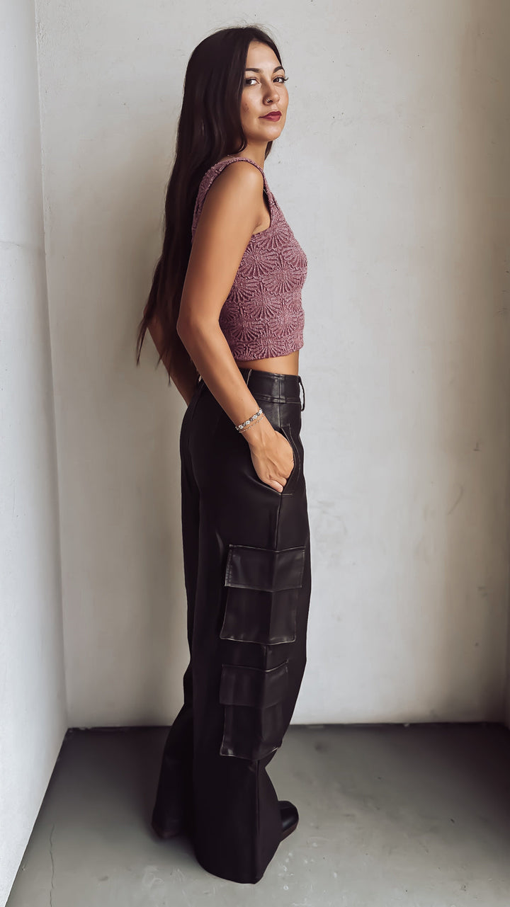 Woman in a purple crop top and leather pants against a white wall.