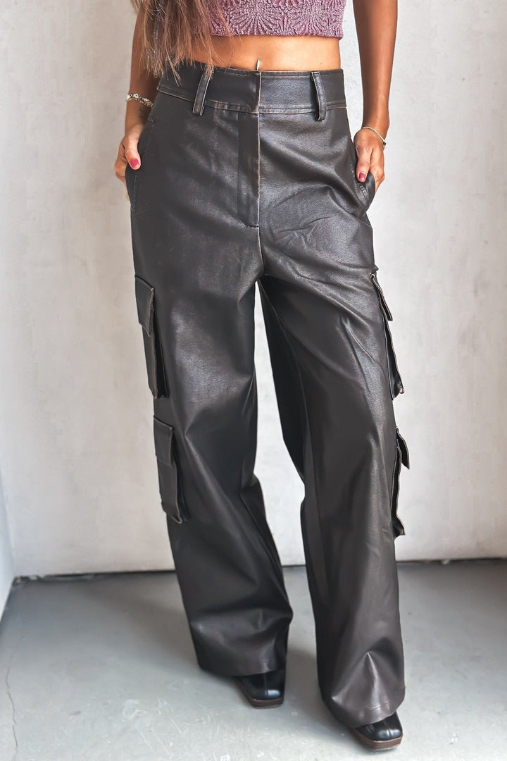 Woman in a purple crop top and leather pants against a white wall.