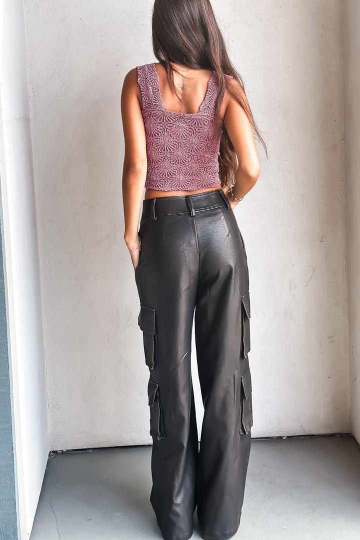 Woman in a purple crop top and leather pants against a white wall.