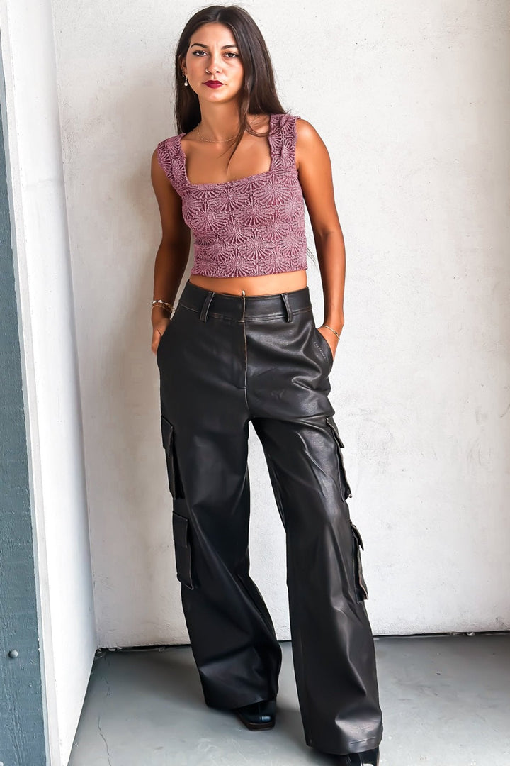 Woman in a purple crop top and leather pants against a white wall.