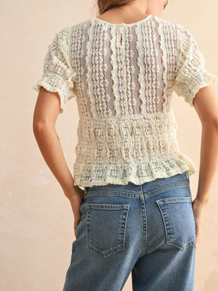 Back view of a white Short Sleeve Lace Blouse with delicate lace, puff sleeves, and scalloped hem paired with denim.