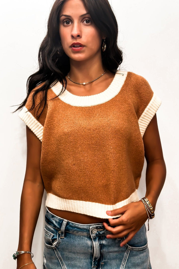 Woman in a cropped brown sweater and denim jeans against a white background.