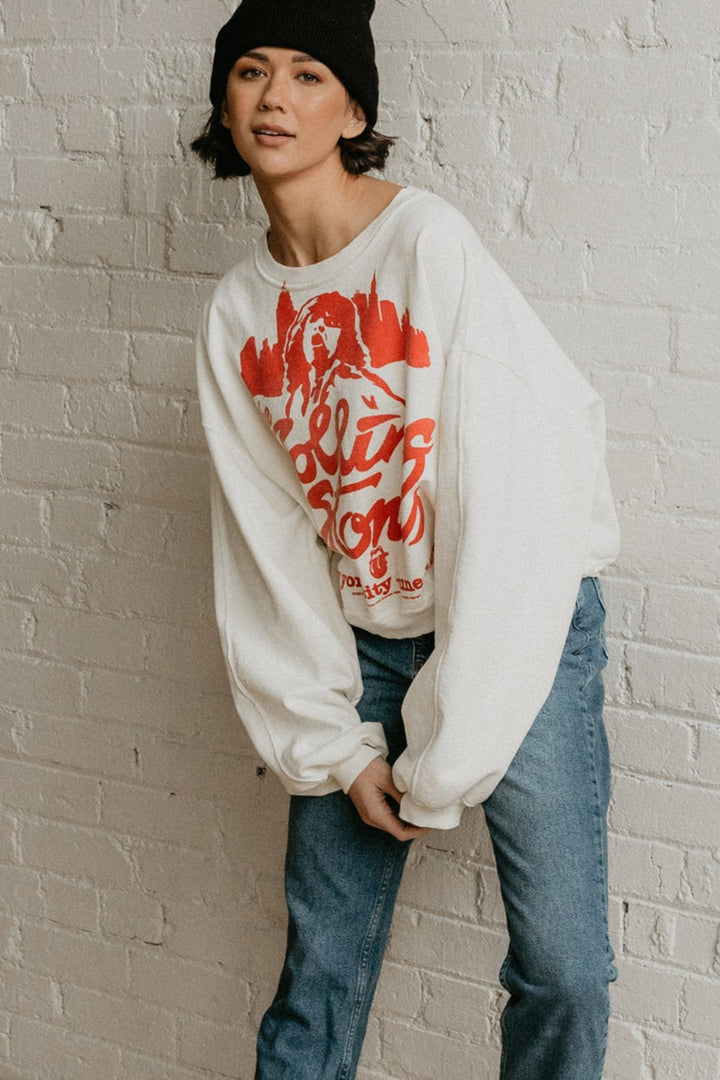 A woman in a white Rolling Stones NYC sweatshirt and jeans looking relaxed and stylish. People of Leisure Sweatshirt