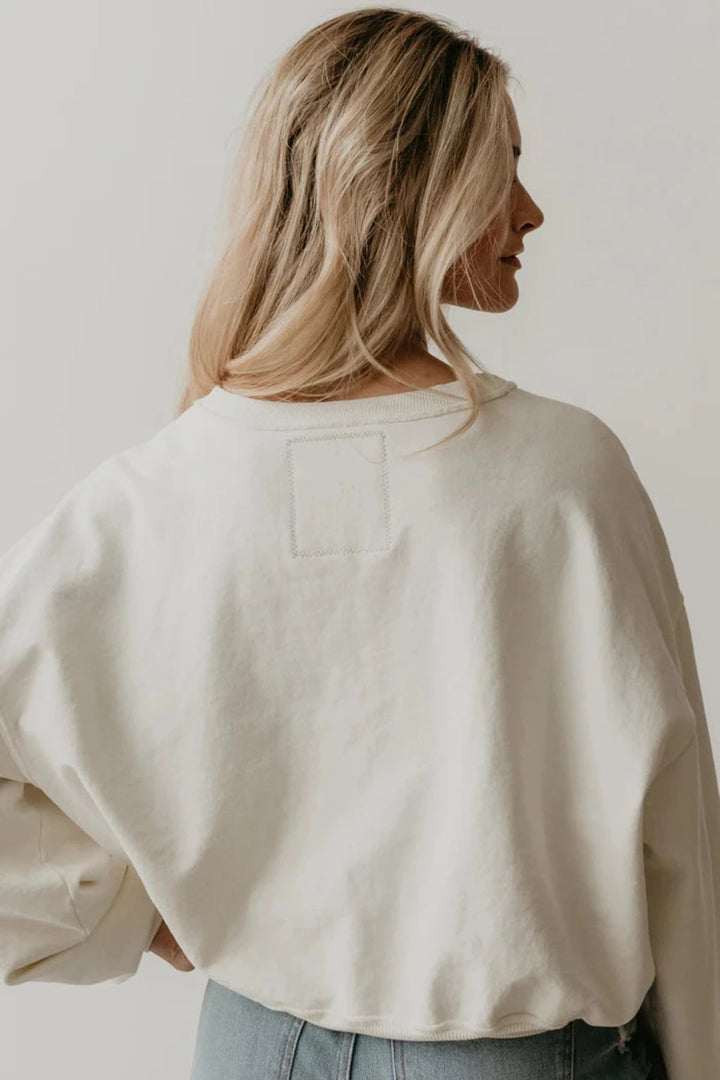 The back view of a woman in a white sweatshirt that features the Rolling Stones NYC graphic 