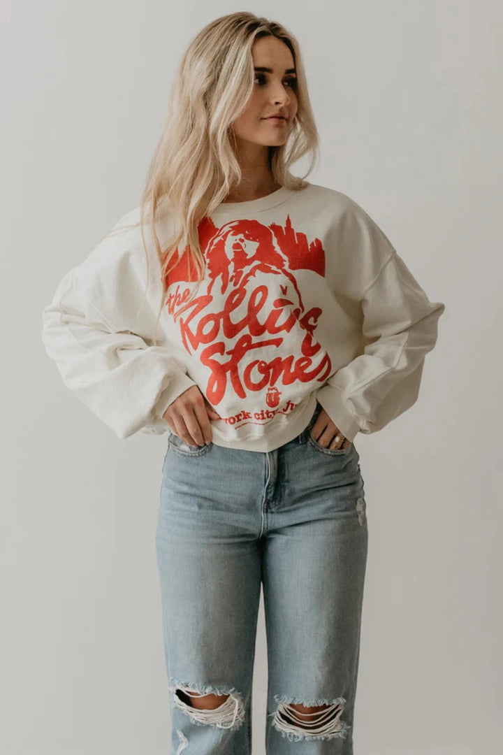 A woman in a white Rolling Stones NYC sweatshirt and jeans looking relaxed and stylish. People of Leisure Sweatshirt