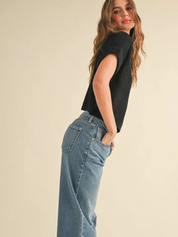 The Capsule Knit Sleeveless Sweater Top on a model in a relaxed black knit paired with jeans.
