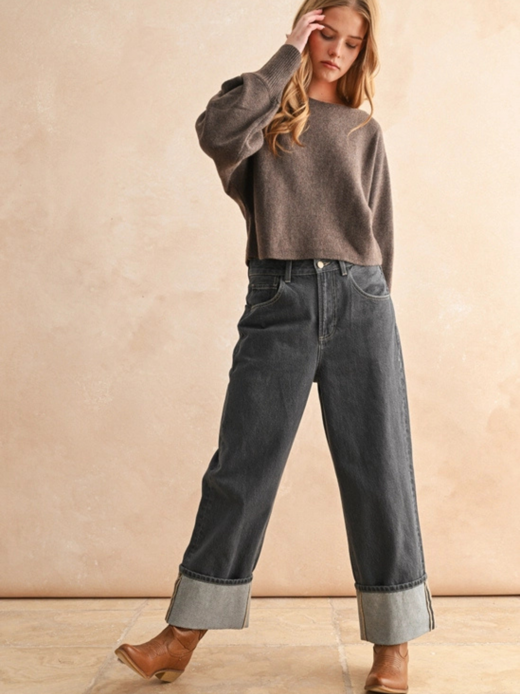 Model wearing The Ella Cozy Boatneck Sweater in taupe knit with dark rolled jeans and tan boots.