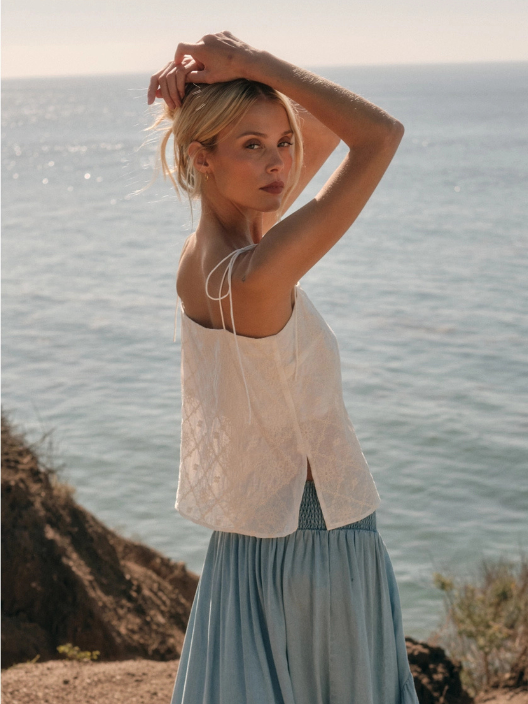The Seafoam Embroidered Cami with delicate floral embroidery, worn by a woman by the sea.