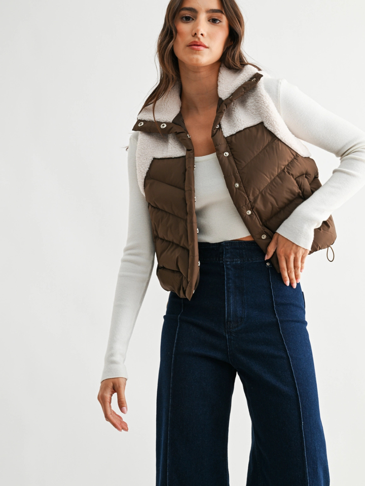 The Willow Sherpa Puffer Vest in brown quilted, plush sherpa collar, layered over a white knit.