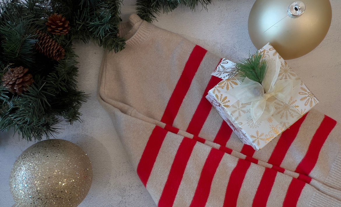 Beige sweater with red stripes on a white surface with Christmas decorations.