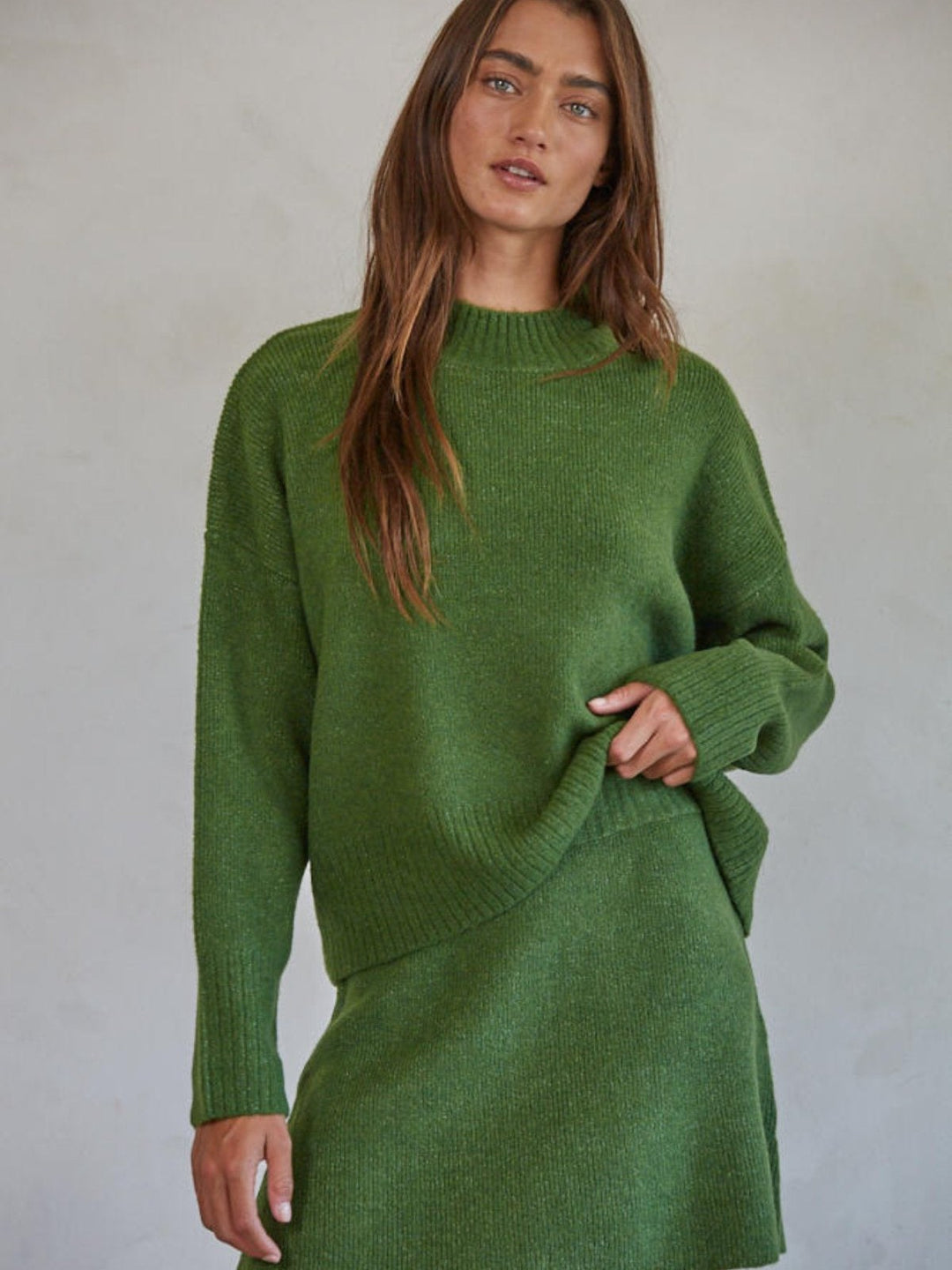 A person wearing a knit sweater and skirt combo with black studded loafers, standing against a neutral background.