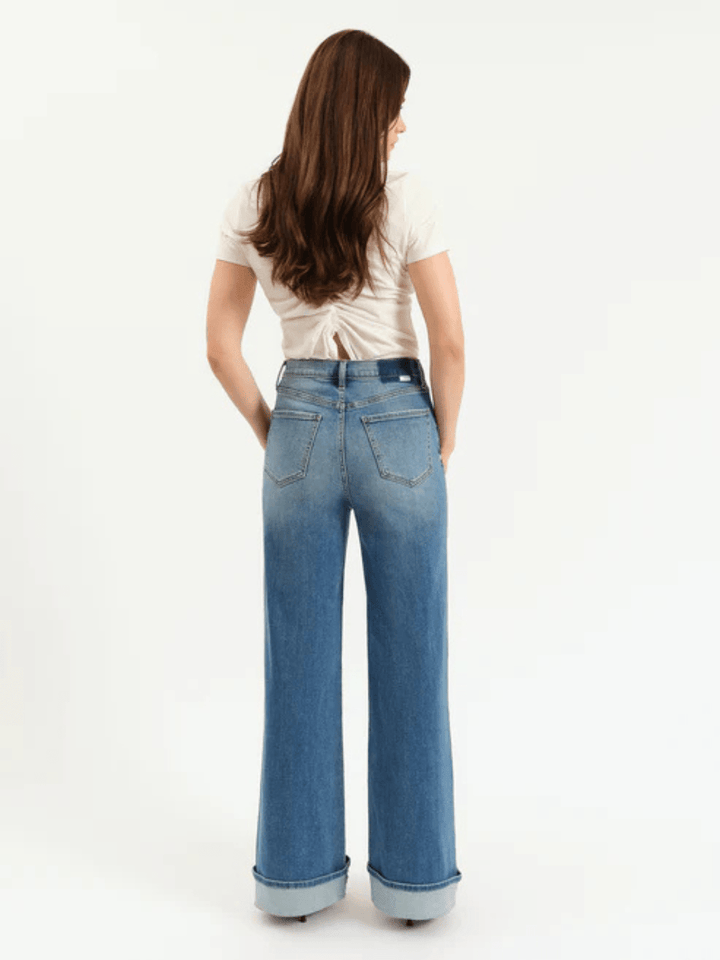 Back view of a model wearing DAZE DENIM Far Out High Rise Wide Leg Jeans in light blue denim with rolled cuffs.