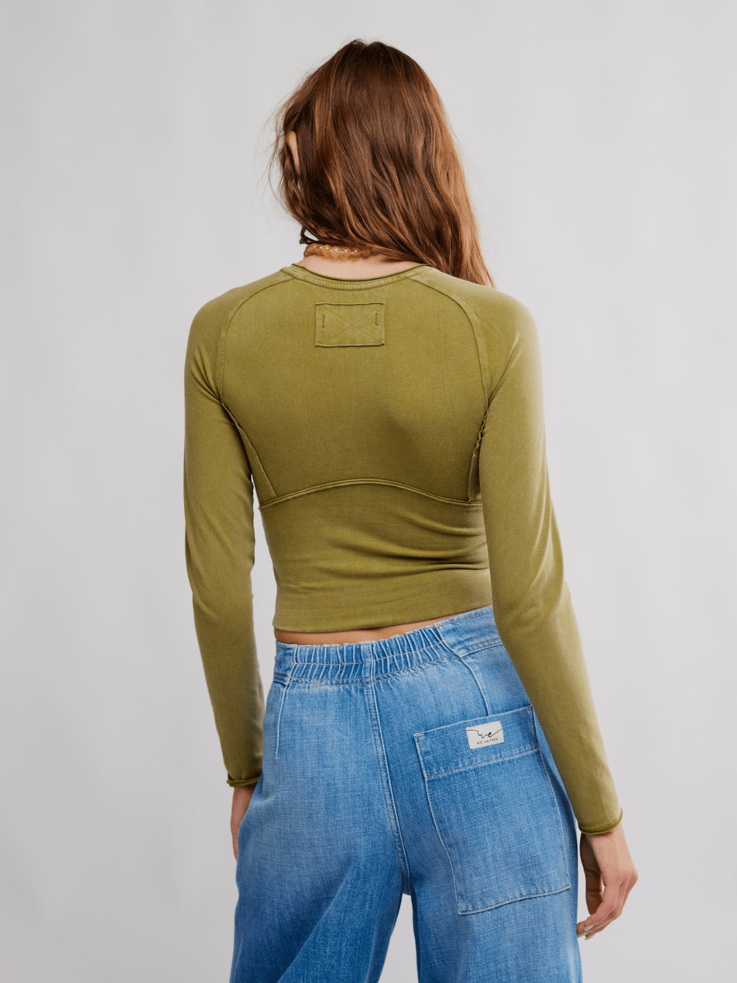 FREE PEOPLE The Protagonist Long Sleeve top, back view on model in olive green with curved seam details.