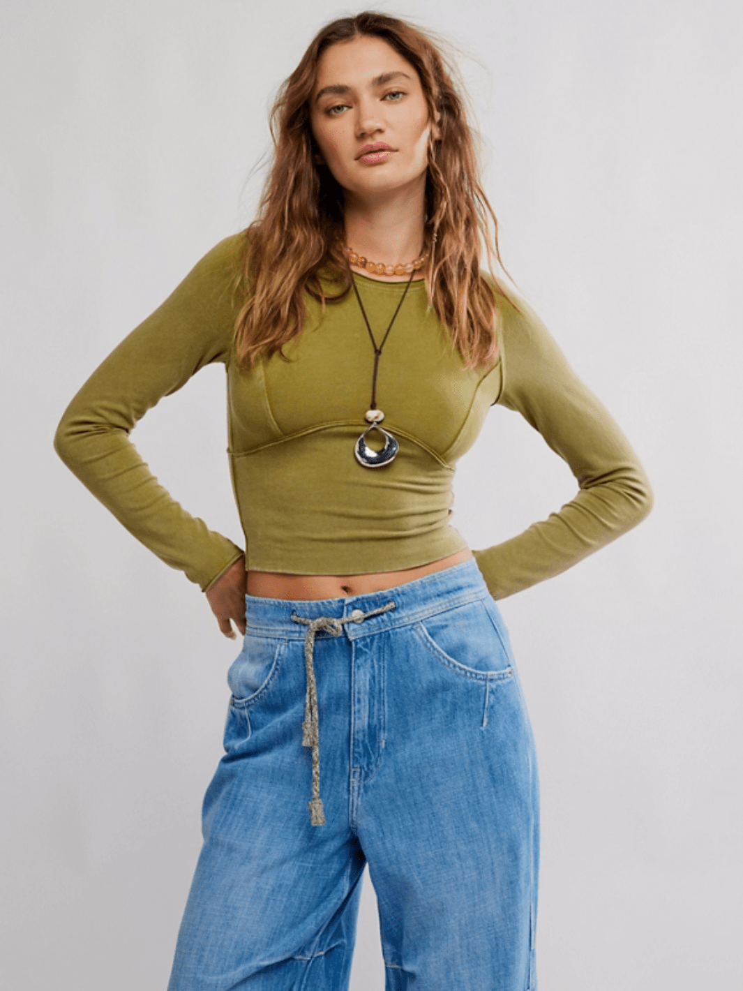 Olive-green The Protagonist Long Sleeve Top on a model, cropped fit with curved seams, paired with light denim jeans.