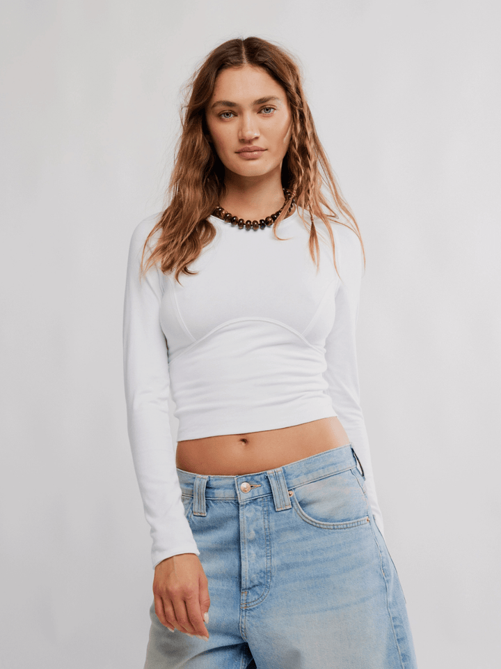 Free People The Protagonist Long Sleeve top in white with a beaded necklace and denim jeans.