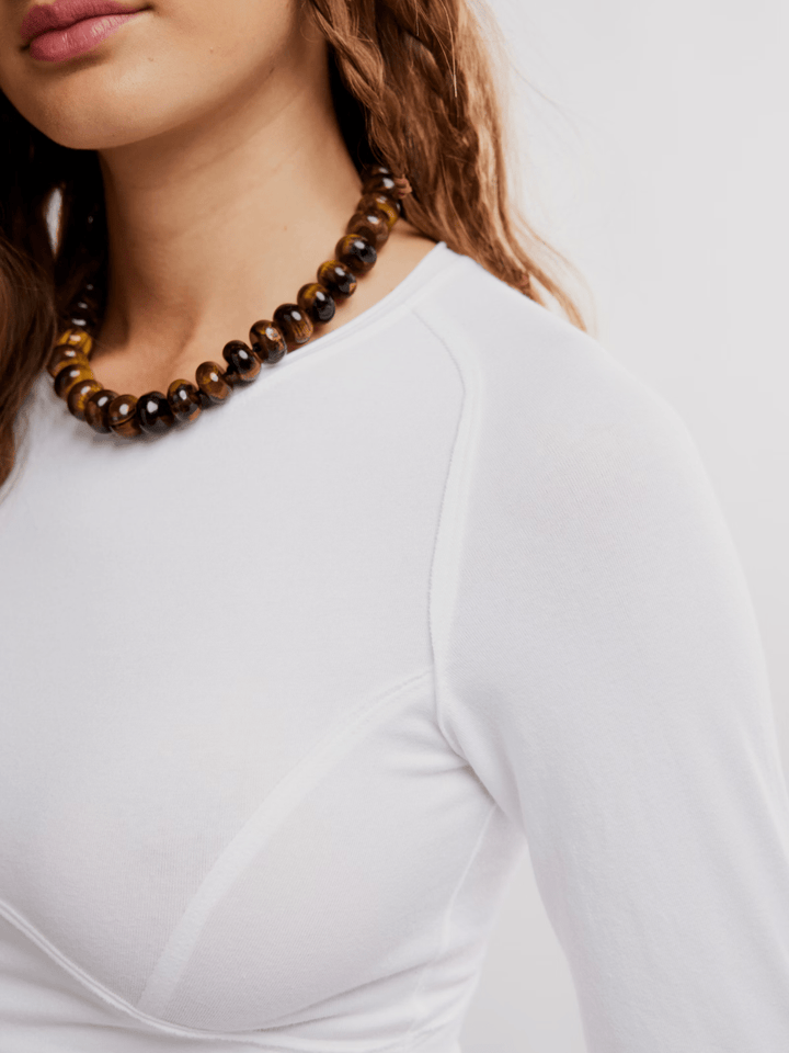 Free People The Protagonist Long Sleeve top in white, close-up of neckline with brown beaded necklace.