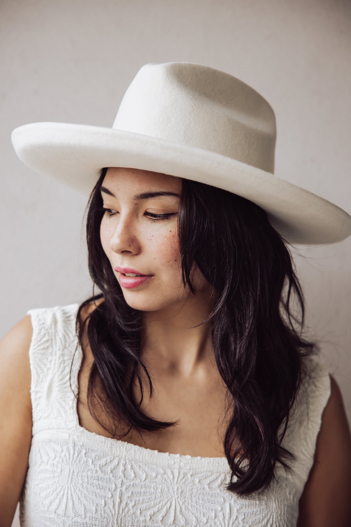 Woman wearing a wide-brim ivory felt hat and a white embroidered top