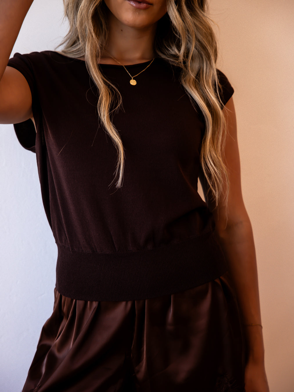 Woman modeling a dark espresso short-sleeve knit top with a gold pendant necklace