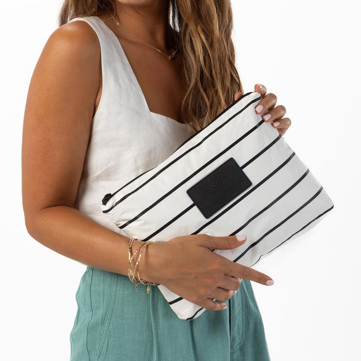 Woman in a white top and sage trousers holding the black-and-white striped Pinstripe Mid Pouch