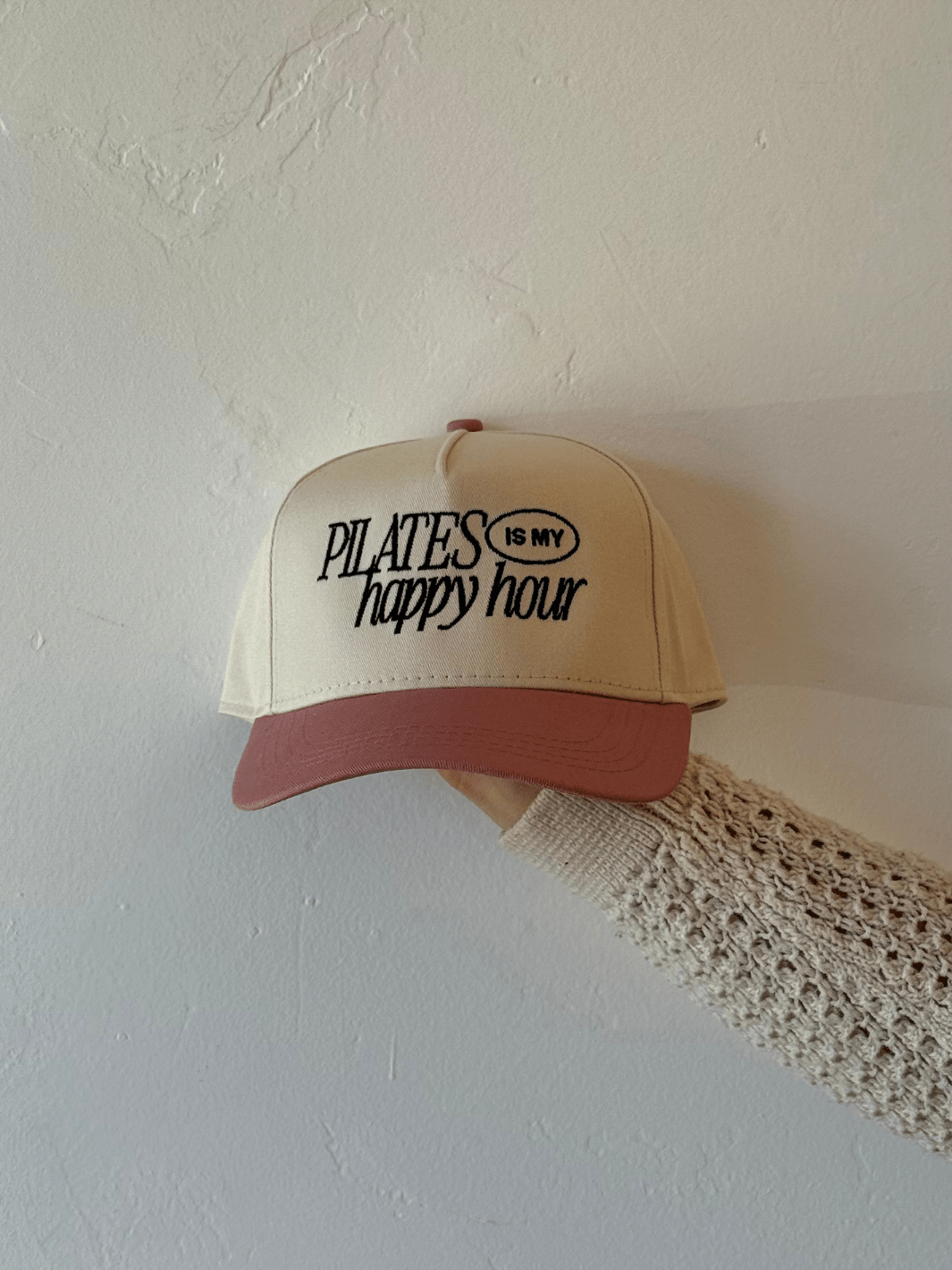 Beige Pilates Is My Happy Hour trucker hat with pink brim and black embroidered slogan.