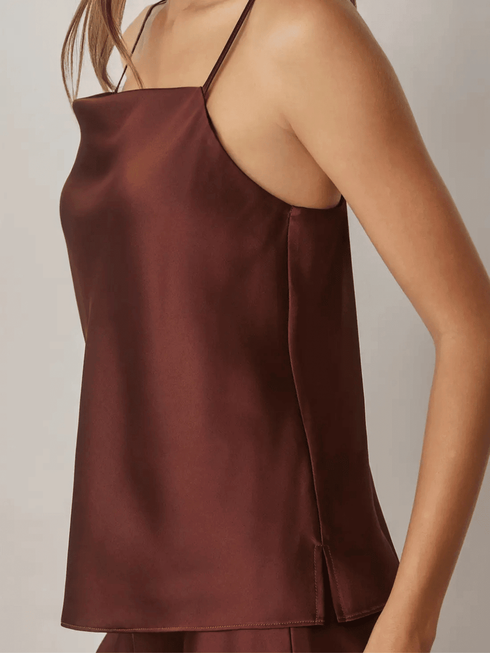 Women wearing a burgundy satin camisole top with adjustable spaghetti straps and a square neckline.